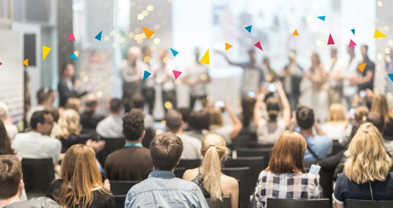 An audience of people seated in an auditorium look on toward a stage of award winners