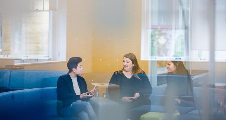 A group of RRU students sit outside a classroom on a blue couch in conversation.