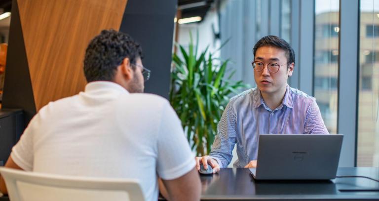 Taejo Kim sits across the desk from a student, in an office environment