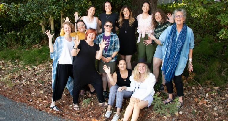 Masters students with Hilary Leighton standing in front of a large tree and waving at the camera.