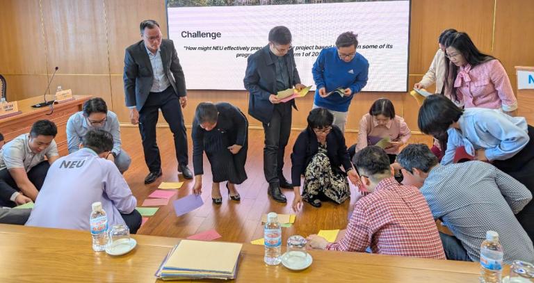 A group of students arrange piece of brightly coloured paper on the floor as part of classroom activity.