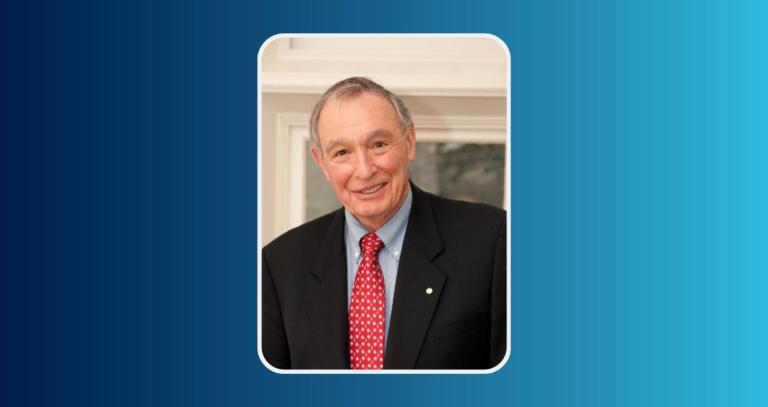 A man wearing a formal blue jacket and shirt offset by a red tie