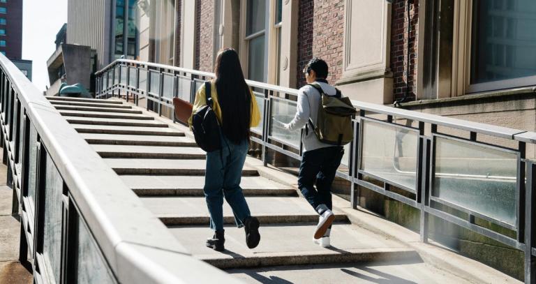 Two university students walk up concrete steps outside in an urban area