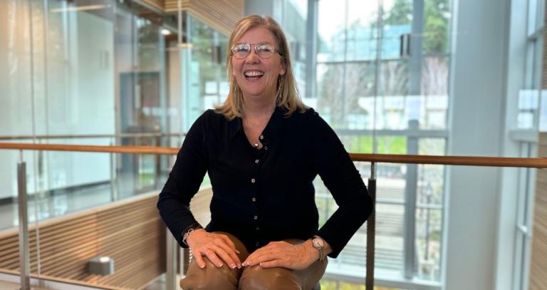 A woman laughs while sitting indoors, in front of a hallway window