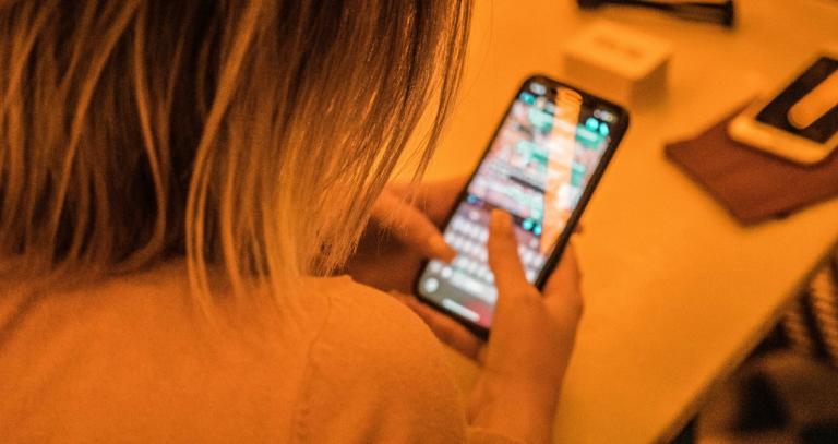 Looking over the shoulder of a woman with short hair, the focus of the image is the cell phone she's holding in her hands.