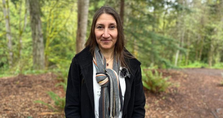 A woman smiles for a head shot, a forested scene behind her.
