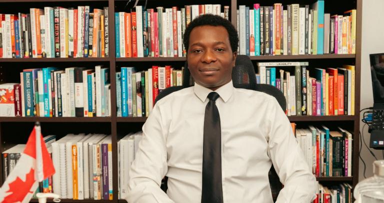 Dapo Bankole sitting in front of a large bookshelf filled with books.