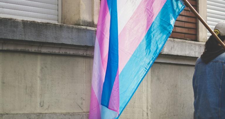 Person walking with a large transgender pride flag hanging over their shoulder