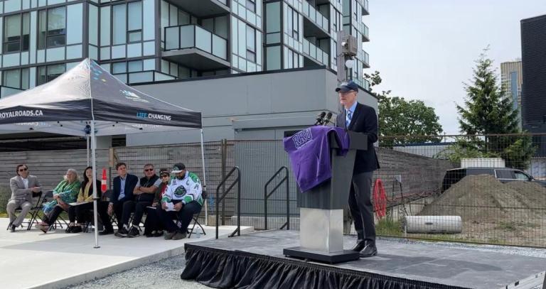 Royal Roads president Philip Steenkamp stands at a podium in front of the new RRU Langford campus