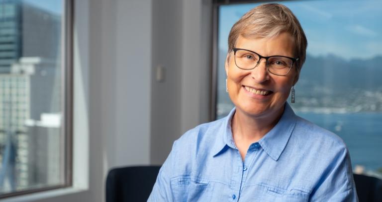 Lori Wanamaker wears a blue collared shirt, has short hair and glasses and is smiling.