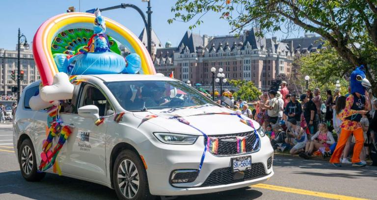Royal Roads white van decorated for Pride with an inflatable rainbow and peacock attached to its roof.