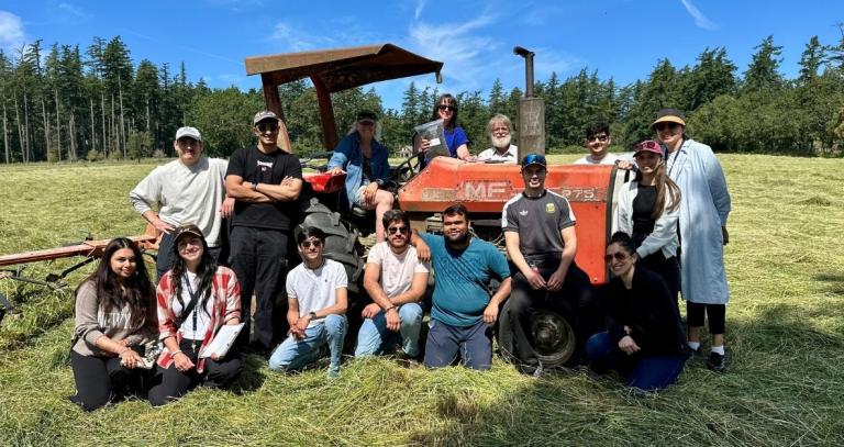 A group of students pose around a tractor on a farm
