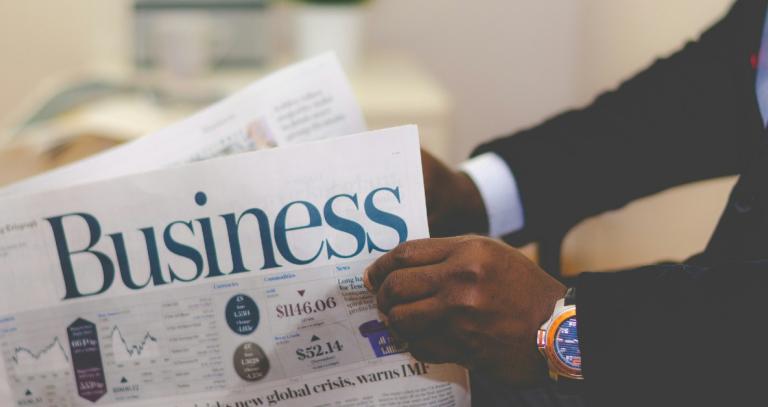 unseen person wearing a suit holding the business section of a newspaper