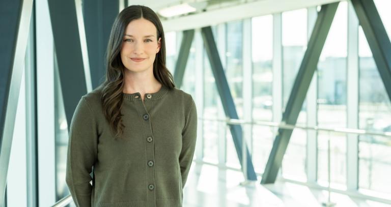 Paige Mason is standing next to a wall of windows wearing a green sweater.