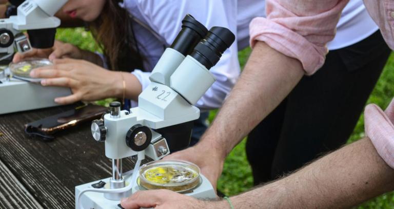 Two students using microscopes to look at specimen in an outdoor setting