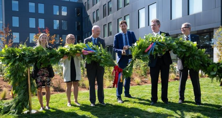 Partner and government representatives join to cut a green cedar bough with large shears