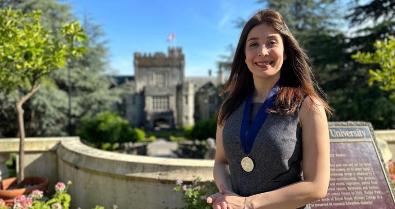 A woman poses with a metal on blue ribbon in front of a stone castle.