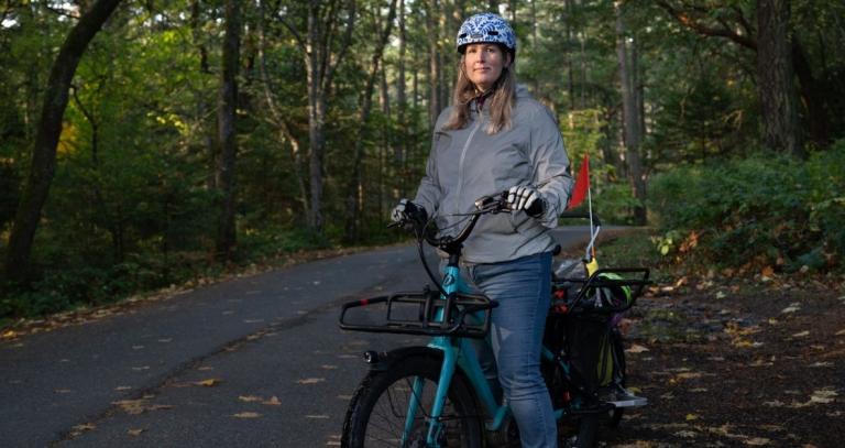 Dr. Julie MacArthur poses with her e-bike alongside a forested road.