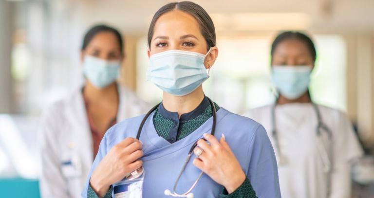 Three nurses stand in a hospital environment wearing scrubs and stethoscopes