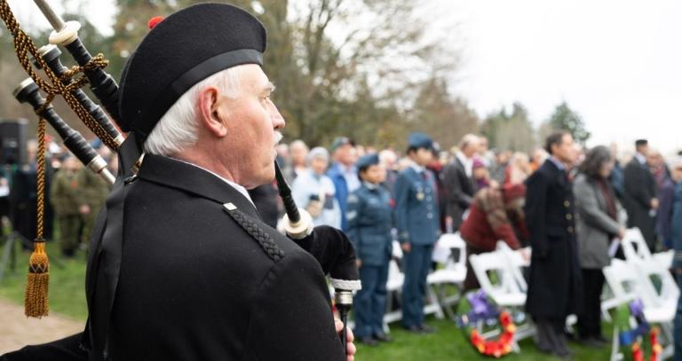 A bagpiper seen from behind while playing for a crowd gathered in remembrance