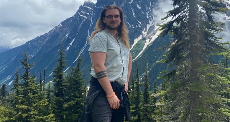 Brian Lawless standing outdoors with mountain peak and trees in the background.