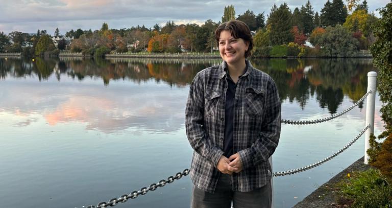 Elisa Paranich stands besides a body of water with trees in the background.