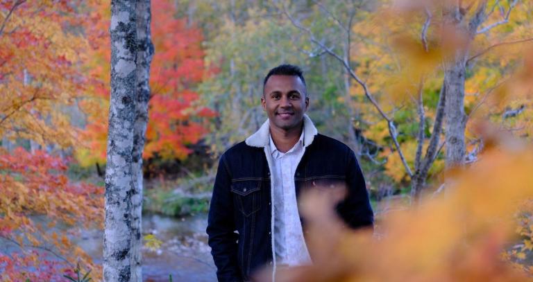 Deny Thomas stands in a forest of fall foliage