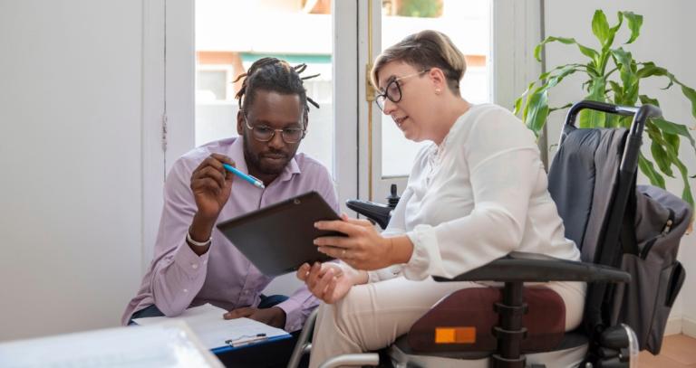 A woman in a wheelchair speaks with a medical professional while looking at an Ipad