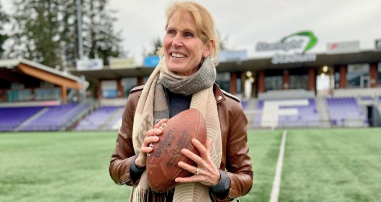 A woman smiles, looking off camera, on a field, holding a football.