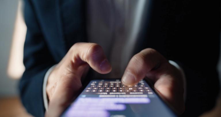 man's hand typing on a smart phone