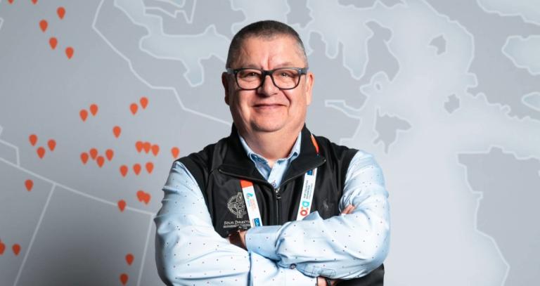 Dan George smiling with arms crossed in front of a map mural