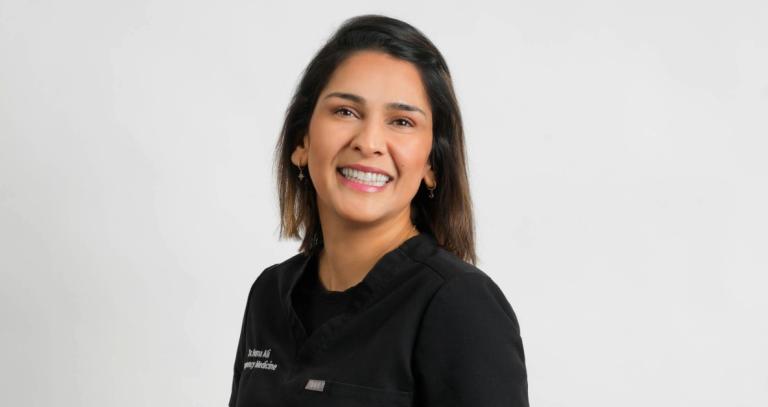 Dr. Huma Ali wearing scrubs and smiling in front of a white background. 