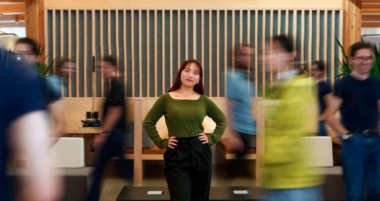 A photo of a woman looking at the camera. The people around her appear blurred by their movement.