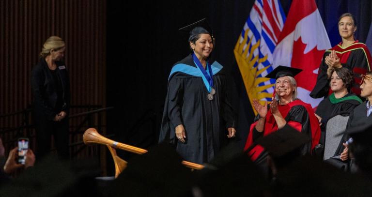 A graduate crosses the convocation stage, wearing two medals.