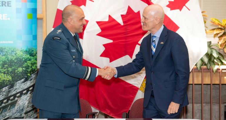 President Philip Steenkamp shakes hands with Major-General Jeannot Boucher, Commander of the Canadian Defence Academy, in front of a Canadian flag