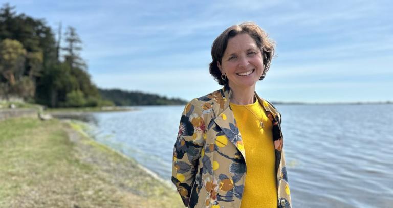 A smiling woman in a yellow top poses on a forested beach.