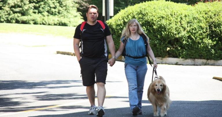 A man and a woman hold hands while walking. The woman holds a dog on a leash.