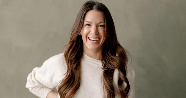 A woman poses for a headshot smiling and leaning in toward the camera.