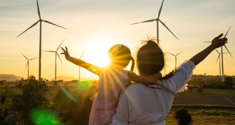 A mother and daughter watch the sunset at a wind farm