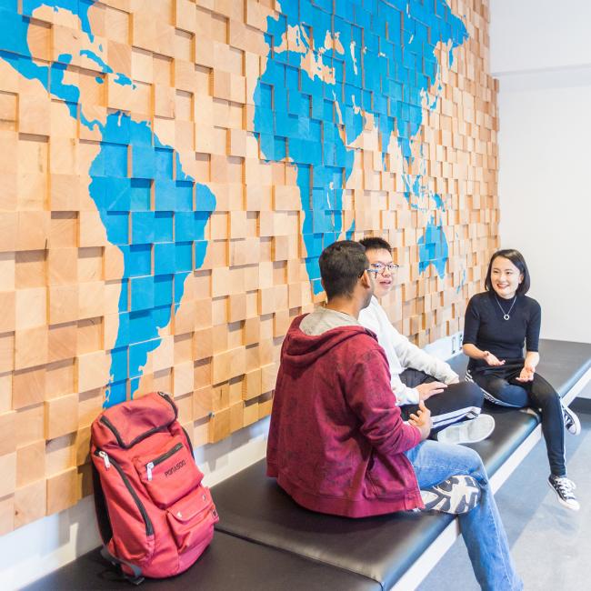 Three-students-seated-in-front-of-wood-panel-world-map