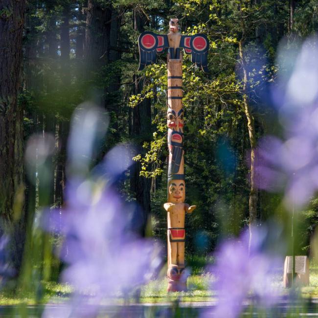 Totem on campus with purple flowers in the foreground.
