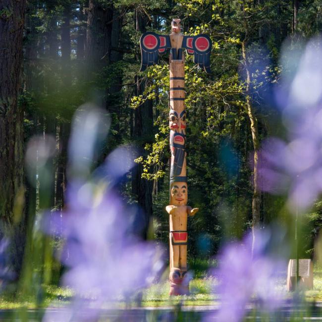 Totem on campus with purple flowers in the foreground.