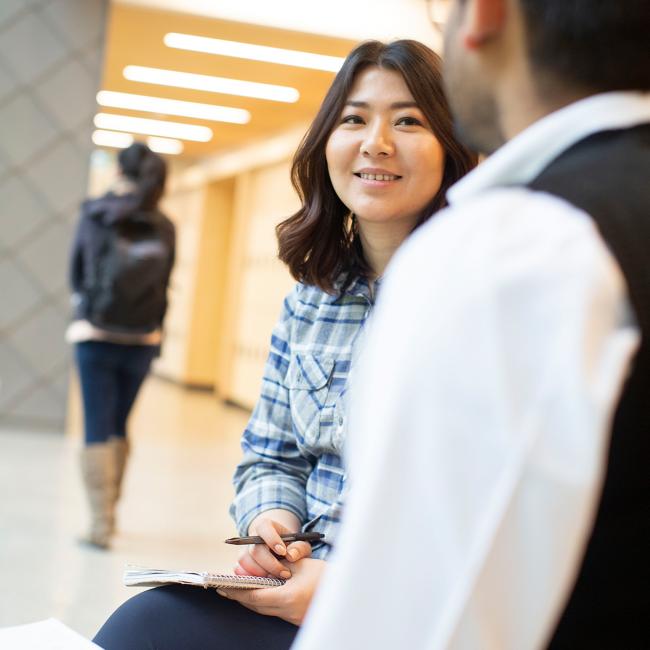 Two-students-seated-talking-in-hallway