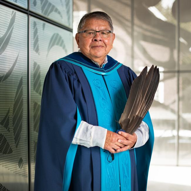 Clarence "Butch” Dick in full blue and teal regalia with his own design holding feathers.