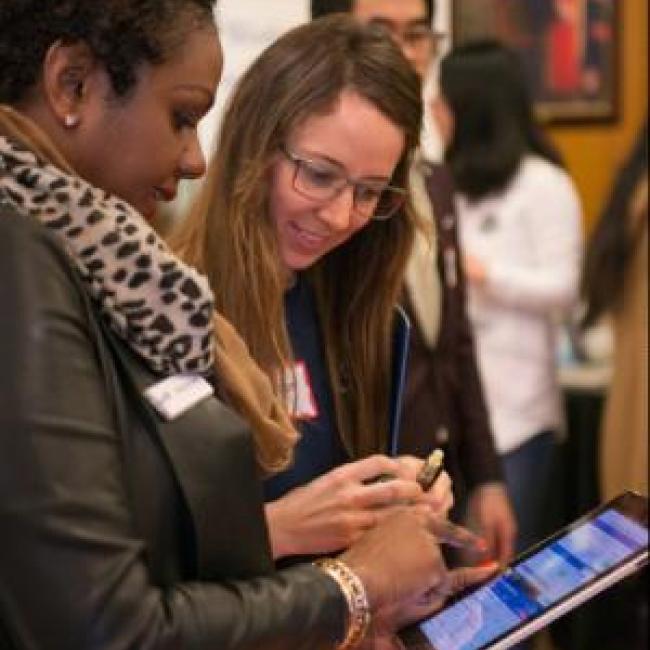 Two people looking at an iPad in a crowded conference room.