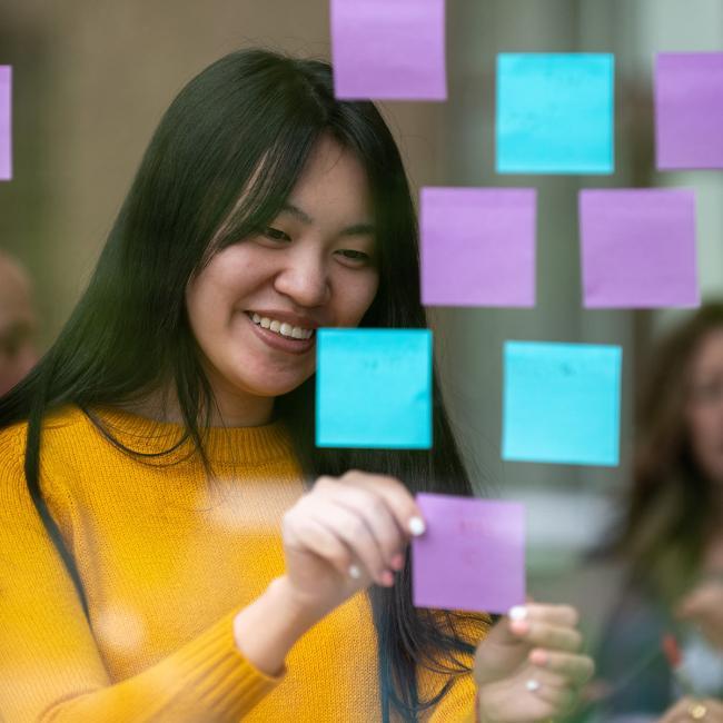 A person smiles as they post sticky notes on a glass wall