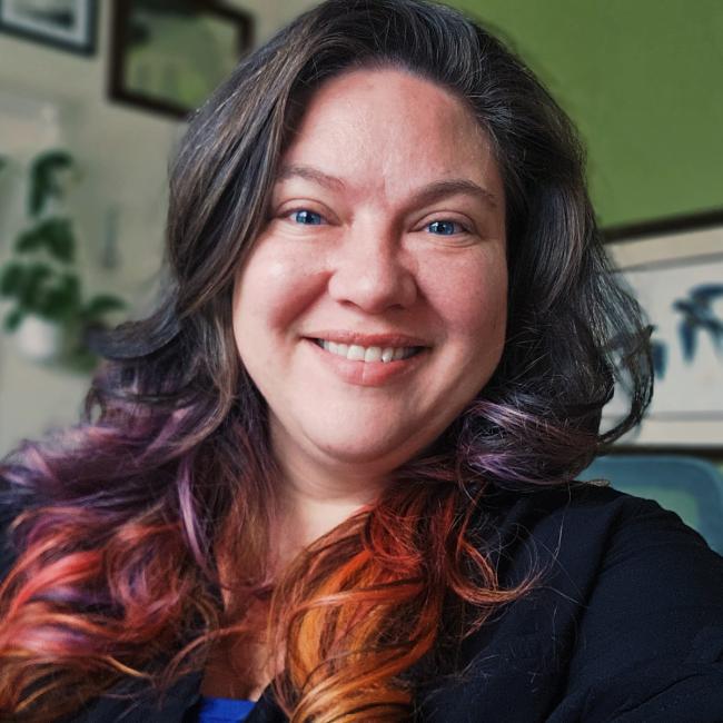Gwen Hill smiles brightly, a tumble of multi-coloured hair falls on her shoulders.