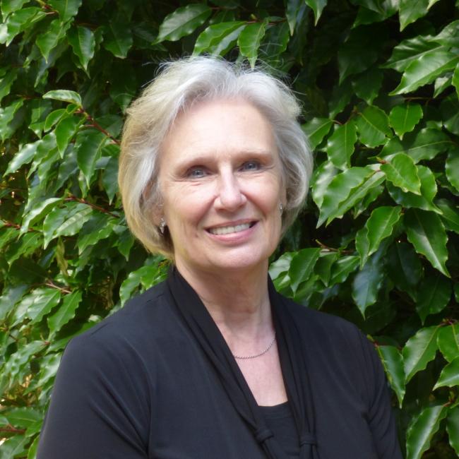 Dr. Jo Axe stands in front of a bright green hedge.