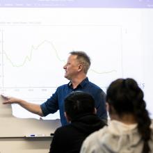 Instructor-pointing-at-graph-on-whiteboard-at-front-of-classroom