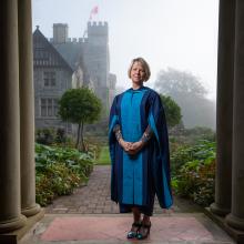 Dr. Bonnie Henry, the Fall 2020 Honorary Degree recipient, stands in a Convocation robe in front of Hatley Castle on a foggy day.